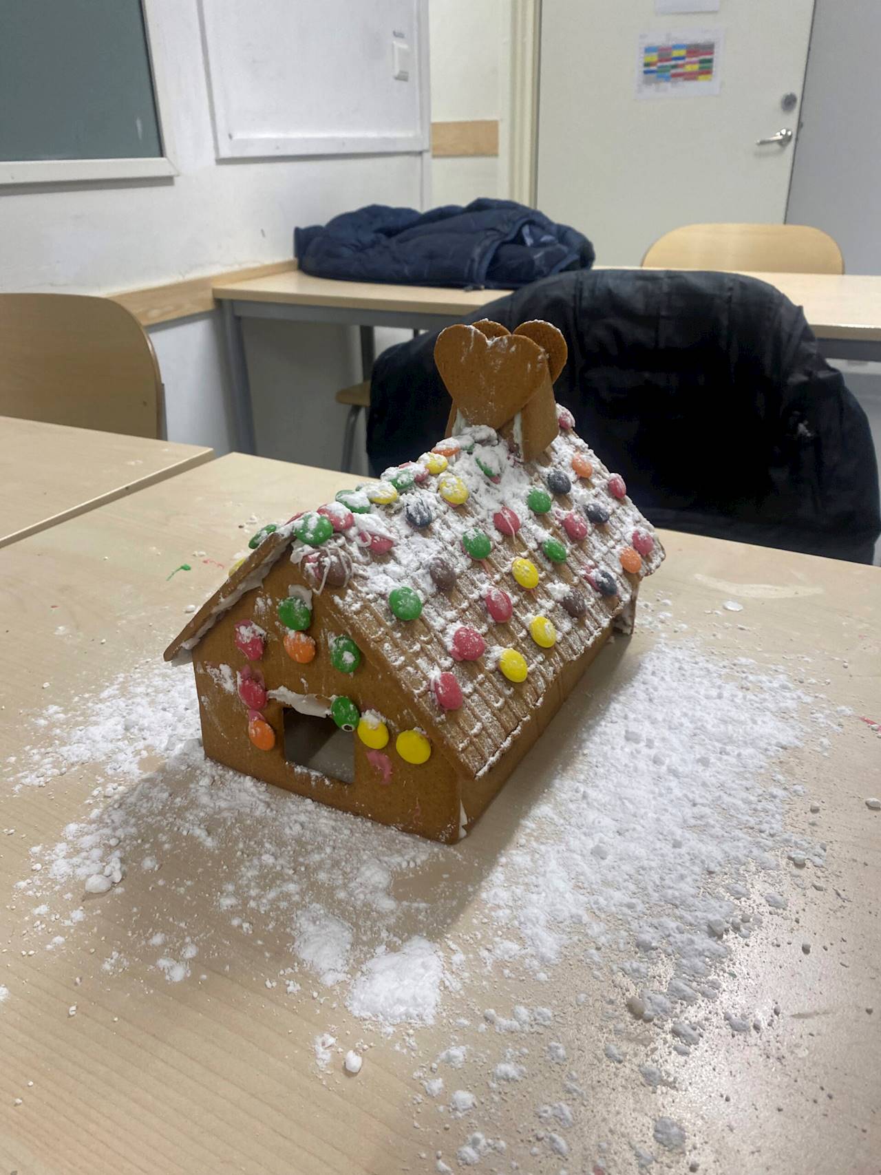 14. Gottsundaskolans MO1-grupp (Uppsala). Bilden föreställer ett pepparkakshus med ett tak klätt i vitt puder, taket är även dekorerat med non-stop choklad i olika färger samt pepparkakshjärtan.
Kantväggen på huset är beklädd med non-stopchoklad.
Pepparkakshuset står på ett bord med vitt puder på.