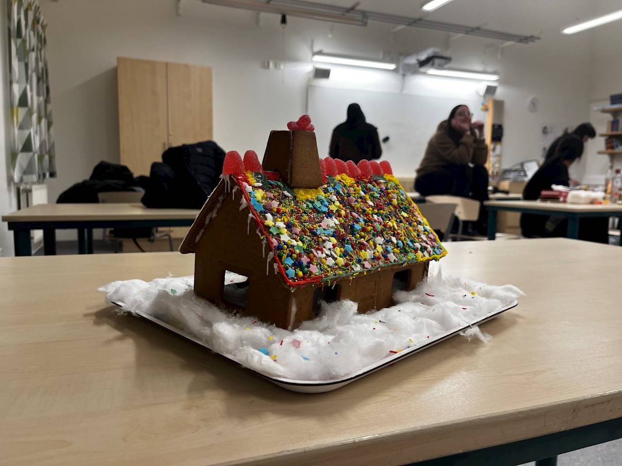 8. Höjaskolan (Malmö). Bilden föreställer ett pepparkakshus på en bricka fylld med vit bomull. Pepparkakshuset har ett tak bestående av glitter i form av stjärnor och andra former, i olika färger. På kanten, på toppen av taket, så finns där rosa gelehallon. På toppen av skorstenen finns där ett enstaka rosa gelehallon.