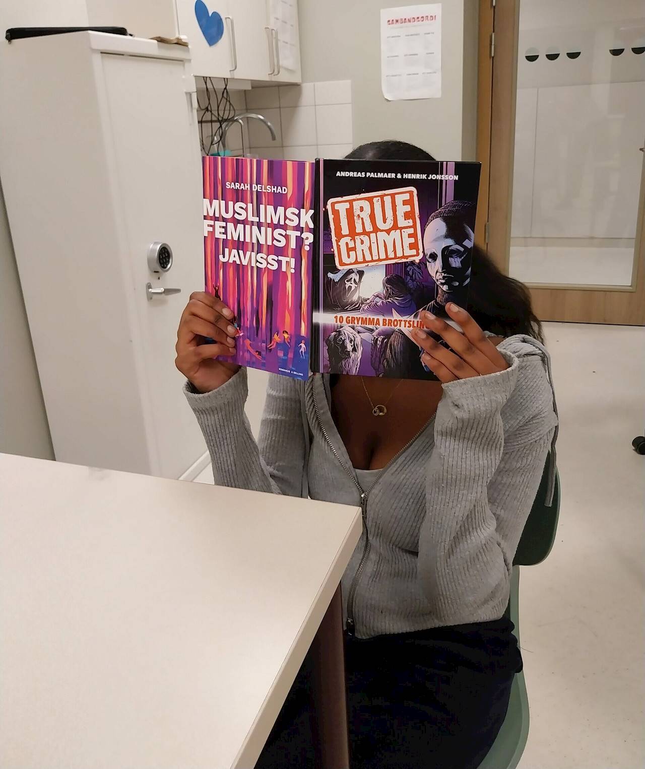 En elev sitter i ett klassrum och håller upp en bok framför ansiktet. På boken står det "True crime".