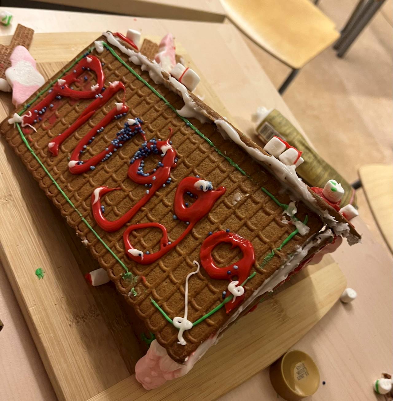 Johannesskolans TT1-grupp (Malmö). Bilden föreställer ett pepparkakshus med "Plugga" skrivet i röd glasyr på takets ena del, delen har även grön glasyr runt dess kanter. Vit glasyr ligger på toppen av taket. Nedanför taket står där en skum-tomte. Vid huset ligger även en tub glasyr.
