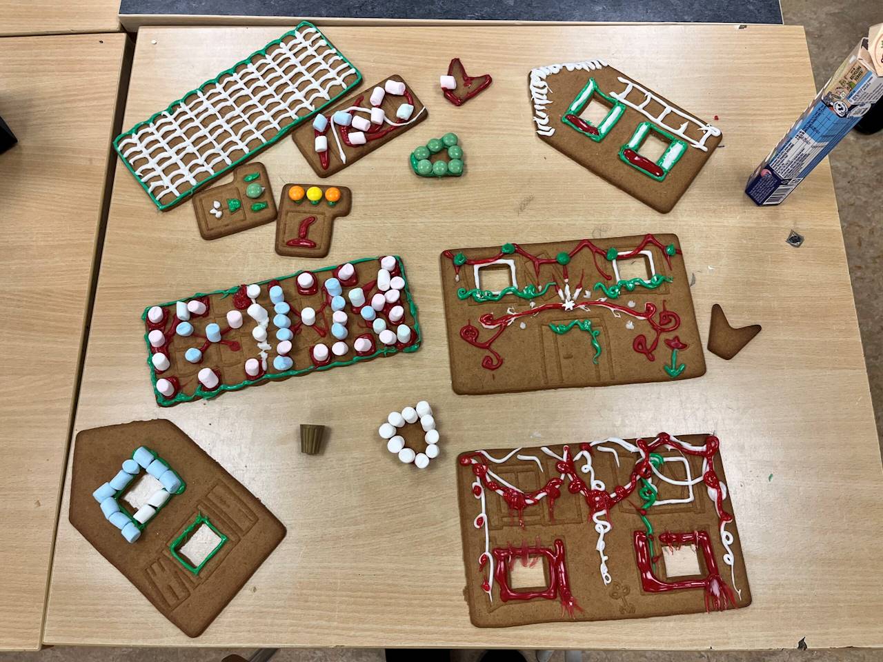 10. Väsby Skola (Uppsala). Bilden föreställer olika icke-sammansatta delar av ett pepparkakshus. Takdelen uppe till vänster i bilden har ett rutnät gjort av vit glasyr, med grön glasyr runt kanterna. Till höger om toppen på bilden finns där en kantvägg med fönster dekorerade i grön, vit och röd glasyr. På kantväggen är det även en stege ditmålad med vit glasyr. På toppen av kantväggen finns där vit glasyr. Runt takdelen finns där hus delar täckta i dekorationer av marshmallows i olika färger, non-stop choklad i olika färger samt röd glasyr.  Takdelen till vänster om mitten av bilden har marshmallows i röd, blå och vit färg fast-klistrat med röd glasyr. 

Höger om mitten av bilden så finns där en husvägg med två fönster, på husväggen är det dekorerat med grön och röd glasyr. 

Längst ner på bilden finns två delar, en kantvägg till vänster som är dekorerat med blå och vita marshmallows runt ett av fönstren, grön glasyr runt kanten på fönstret under. 

Till höger på nedre delen av bilden finns en långvägg som är dekorerad i röd, vitt och grön glasyr. Den röda glasyren är runt fönsterkanterna. 

Delarna ligger allesammans på ett bord.