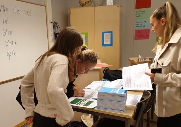 Tre personer tittar igenom elevkontrakt och målböcker som ligger staplade på ett bord i ett upplyst klassrum