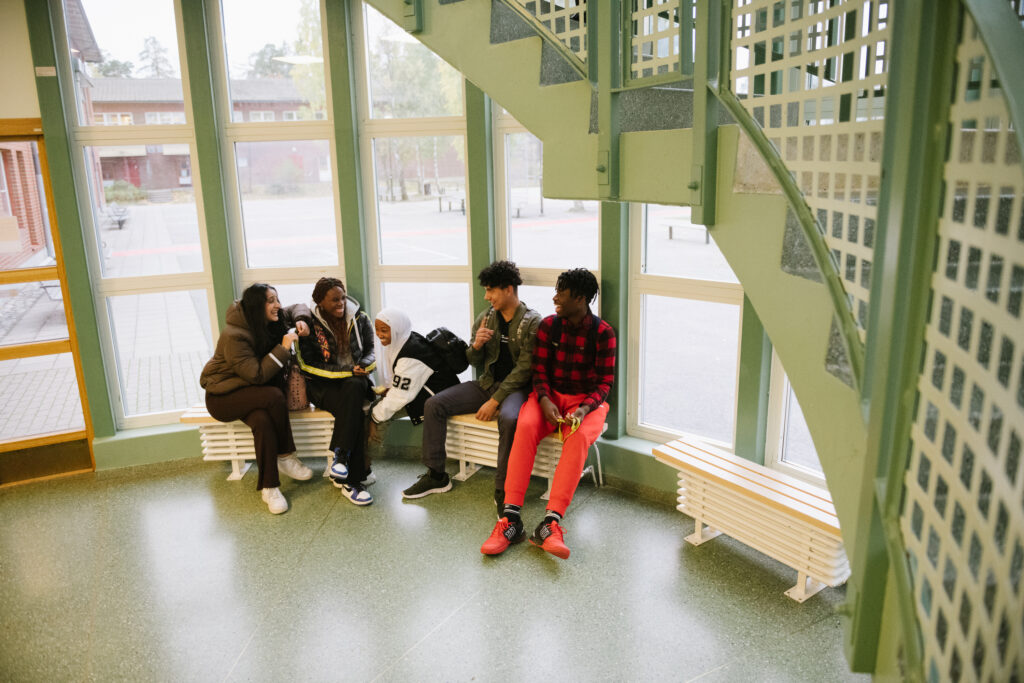 Fem elever sitter på en bänk i en grön skolmiljö på Annerstaskolan och tittar på varandra och skrattar