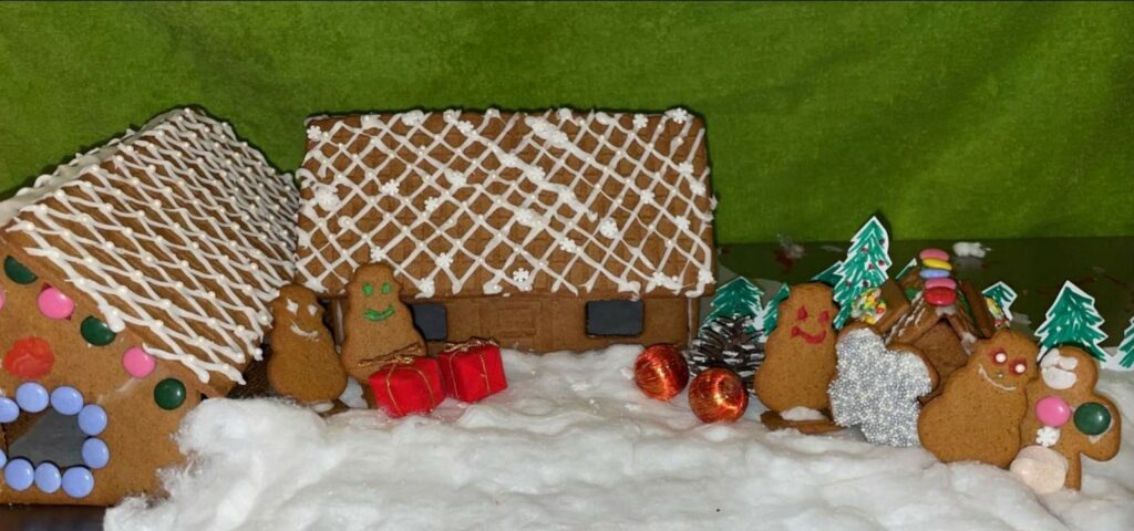 Grön bakgrund med ett pepparkakhus med rutigt tak gjort av glasyr. Framför huset syns pepparkaksfigurer med glada ansikten, ett par röda julklappar och granar ritade i tuschpenna.