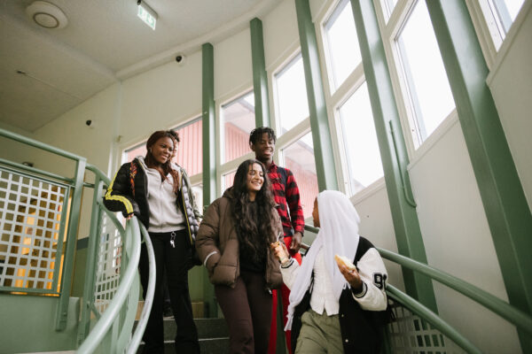 Fyra elever går ner för en trappa i en skolbyggnad och tittar på varandra och skrattar
